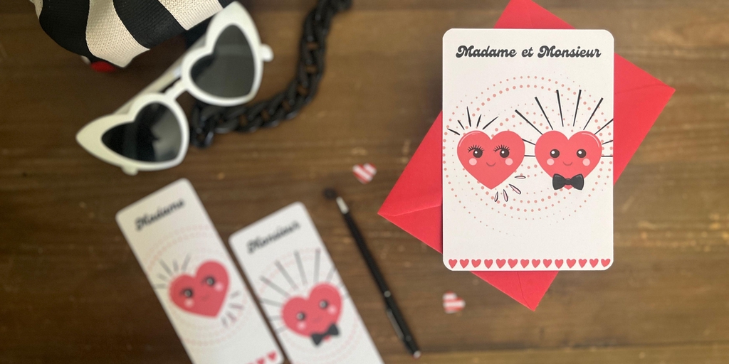 La carte mariage "Madame & Monsieur" est posée sur un meuble en bois. A côté d'elle on retrouve les marque-pages assortis : celui pour Madame et celui pour Monsieur. Les lunettes de soleil blanches en forme de cœur sont posée juste à côté de l'ensemble de papeterie. Les illustrations de ces créations sont dans un style rétro pop, des cœurs rouges avec des visages heureux et souriants, un nœud papillon noir pour Monsieur et des longs cils pour Madame. Les couleurs sont rouge, noir et écru. Au dessus du couple de cœurs on retrouve l'inscription "Madame & Monsieur" dans une police d'écriture très seventies. Tout en bas, une ligne de cœurs rouges.