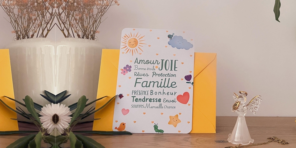 carte baptême avec son enveloppe jaune vif. La carte est illustrée avec de jolis petits dessins enfantins : soleil, nuage, étoile, oiseaux, cœurs, fleurs, chenille, coccinelle. Les couleurs sont douces et lumineuses à la fois. au centre des mots de couleur vert sauge sont écrits dans différentes polices d'écriture : amour, joie, bonne étoile, rêves, protection, famille, présence, tendresse, bonheur, envol, sourires, merveille, chance. La carte est posée sur une étagère avec un petit ange en cristal, des fleurs séchées, une plante et une branche d'olivier.