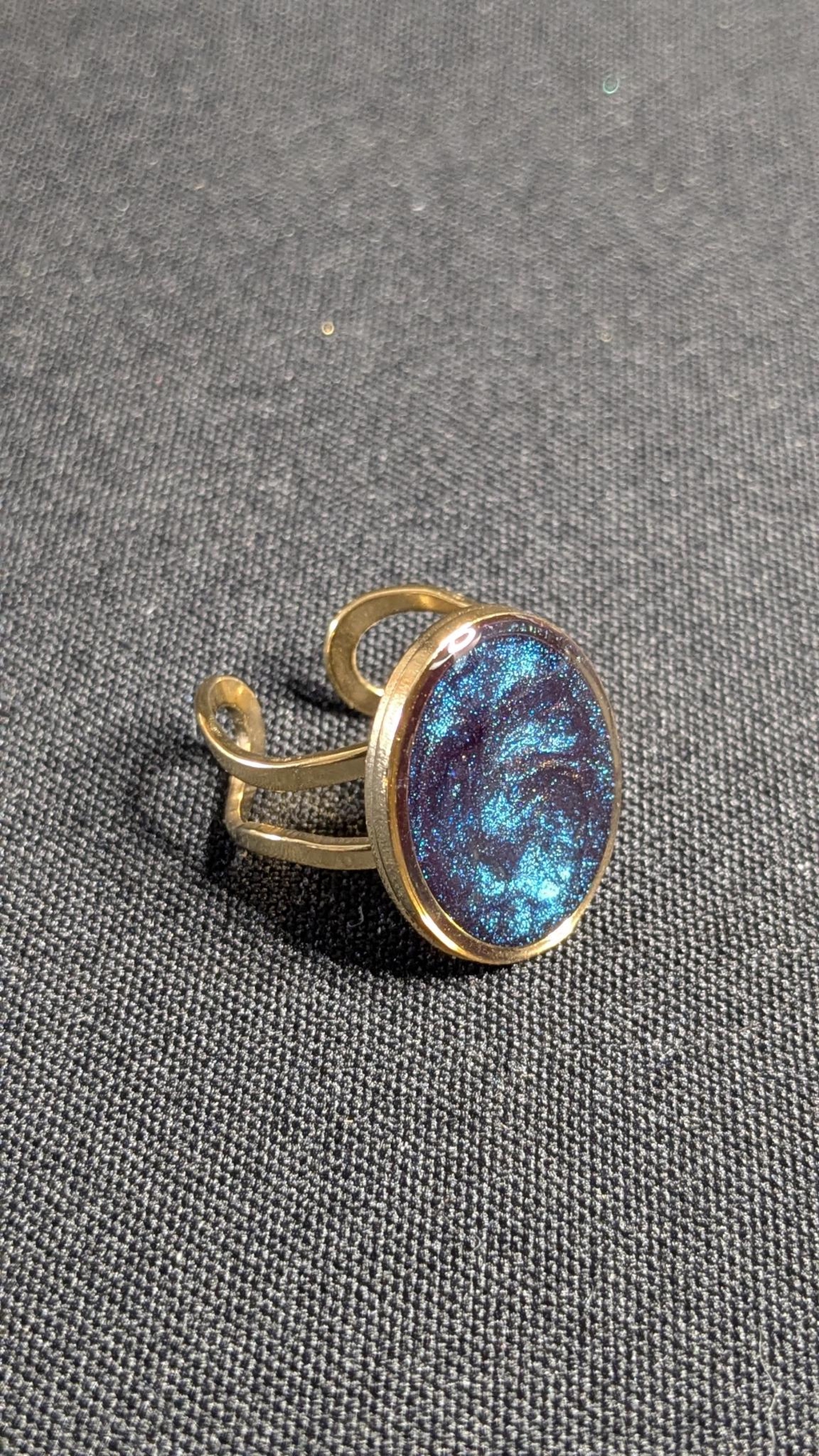 Une photo d'une bague dorée sertie d'une pierre de résine pailletée.