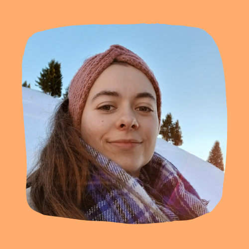 Portrait d’une personne souriante en extérieur, avec un bandeau rose et une écharpe, devant un paysage enneigé.