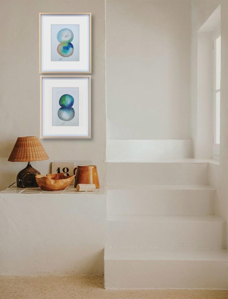 Une œuvre représentant deux formes circulaires aux tons bleus, verts et gris  est accrochée au mur blanc d'un intérieur épuré et lumineux