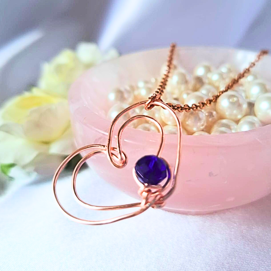 Bijou de créateur : collier acier inoxydable plaqué rose doré, façonné à la main en forme de double coeur, serti d'un cristal de verre bleu profond