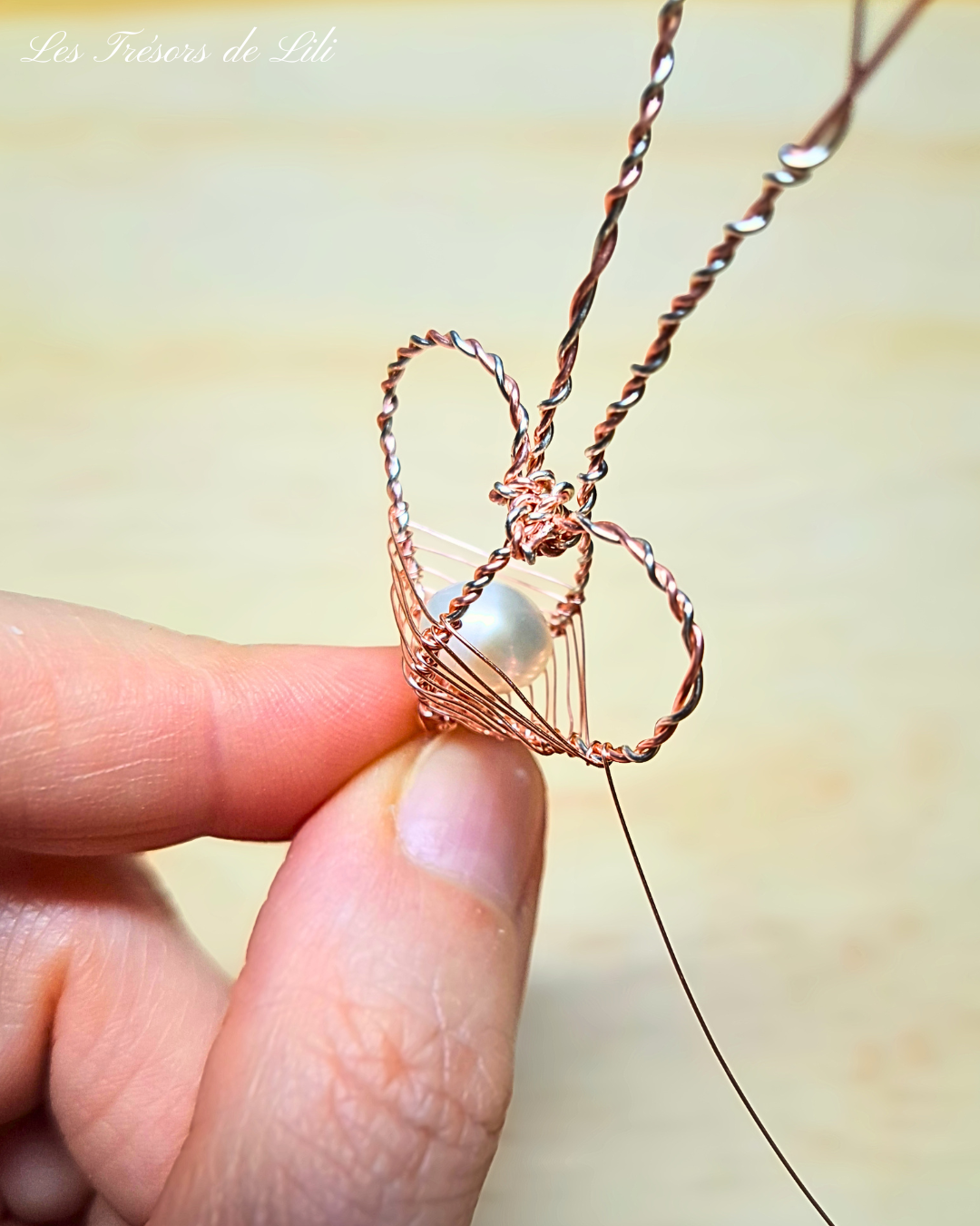Création en atelier d'un bijou de créateur : pendentif en forme de coeur, tissé main en volume avec du fil de cuivre argenté et rose doré, et renfermant une perle d'eau douce blanche