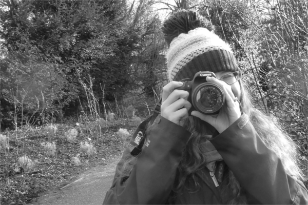 Image of women in bobble hat and coat taking a photograph with a DSLR camera