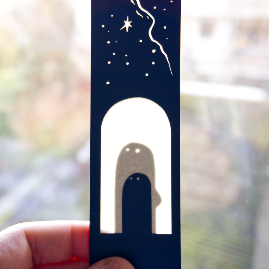 Un marque-pages bleu nuit montre un personnage se tenant sous une voute étoilée. Un jeu de transparence permet de voir un second personnage qui se tient à ses côté, lorsqu'on le place à la lumière.