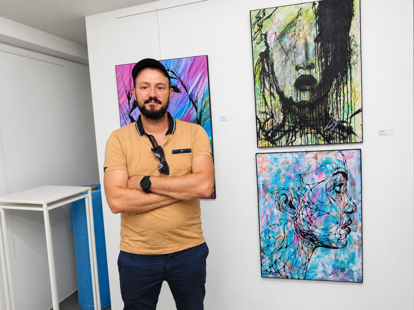 Tony Debs posant dans une galerie devant plusieurs œuvres contemporaines exposées