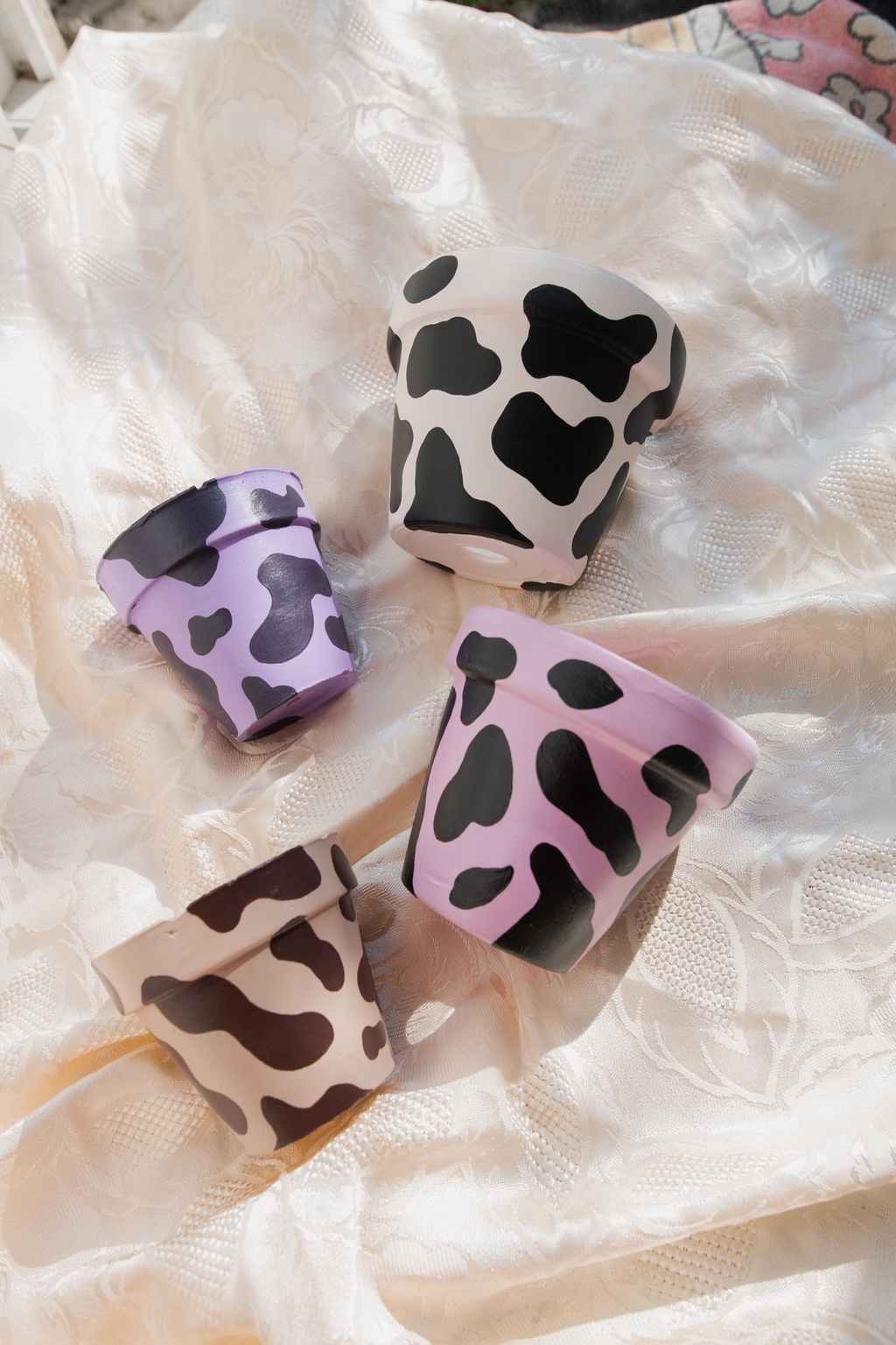 Pots peints à la main, empilés pour révéler un festival de motifs et de couleurs : damier, vache, coeurs, nuages et formes arrondies. Du rose au noir, en passant par le doré et le violet, chaque pot est unique pour apporter personnalité et bonne humeur à ton intérieur.