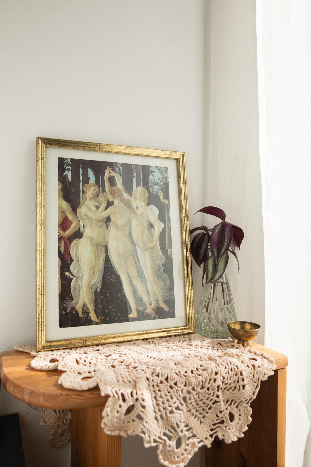 Inspiration décoration goth et végétale : une étagère en bois décorée d’un cadre Botticelli, d’une bouture de misère dans un vase et d’un napperon délicat. Idée pour associer art, plantes et touches vintage dans un intérieur.