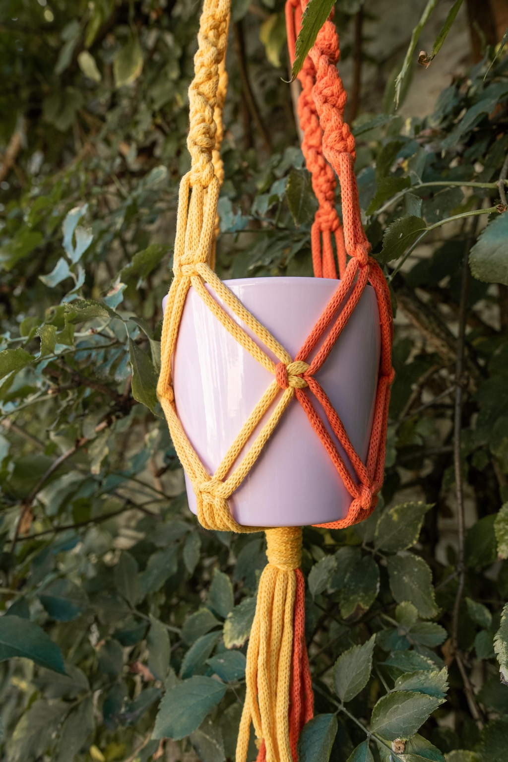 Macramé violet orné de perles, accompagné de pots colorés violet et orange et de feuilles décoratives. Parfait pour apporter une touche bohème et originale à ton intérieur, tout en mettant en valeur plantes et accessoires déco.