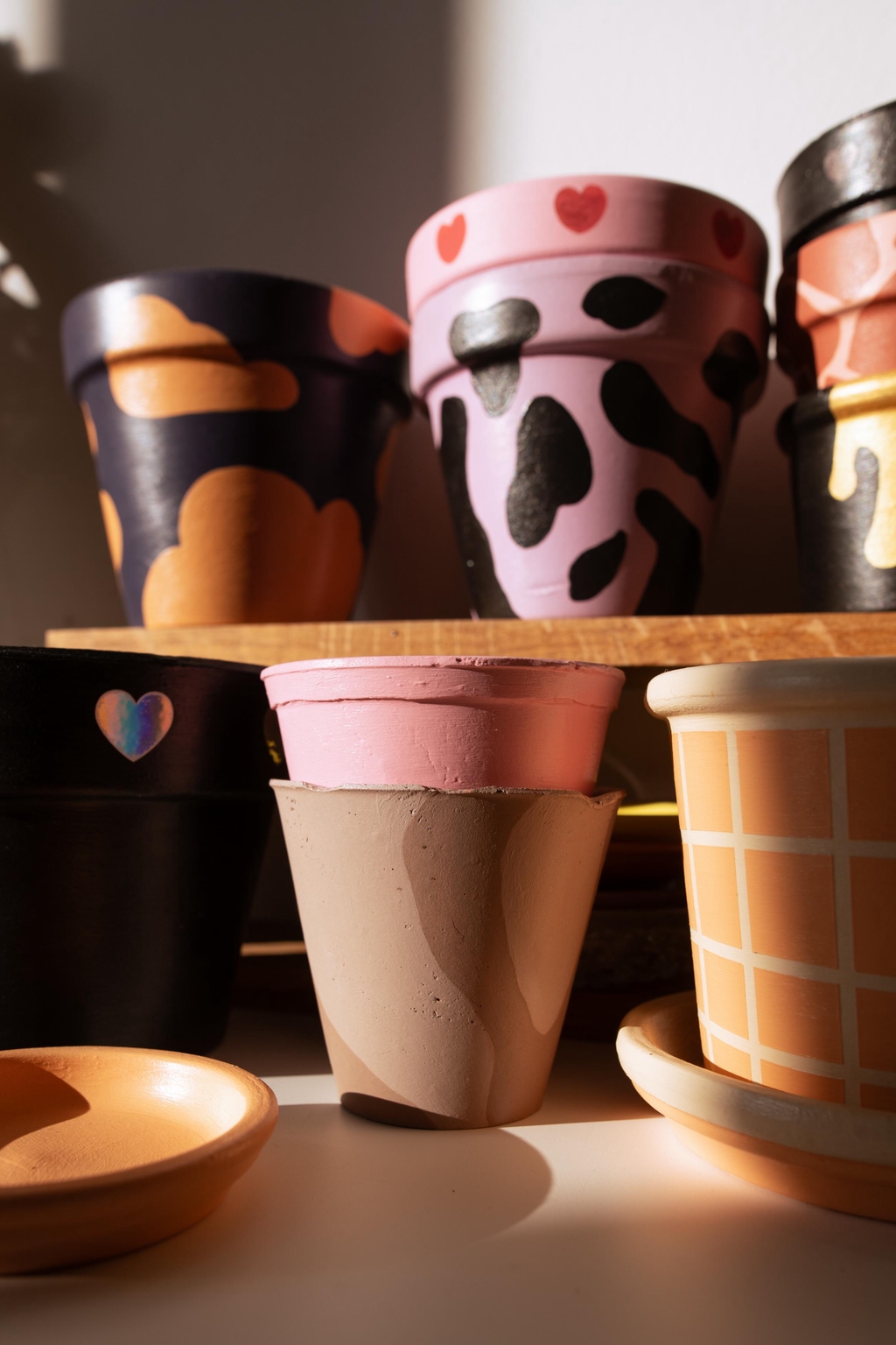 Pots peints à la main, empilés pour révéler un festival de motifs et de couleurs : damier, vache, coeurs, nuages et formes arrondies. Du rose au noir, en passant par le doré et le violet, chaque pot est unique pour apporter personnalité et bonne humeur à ton intérieur.
