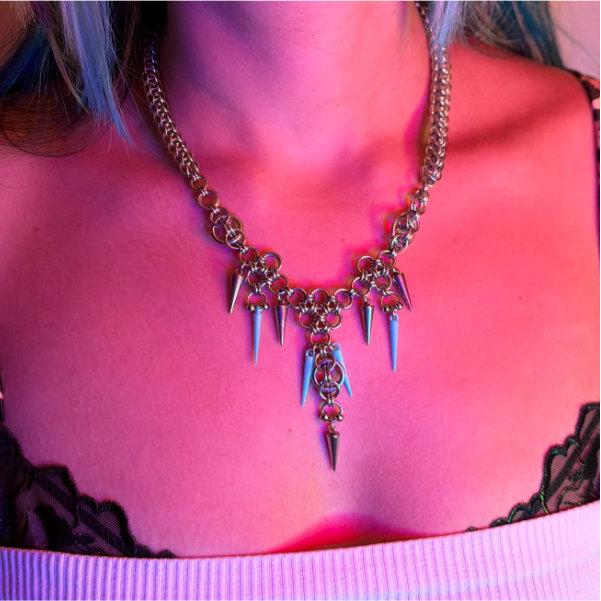 A chainmaille necklace on a womans neck with blue spikes, there are pink and blue tones