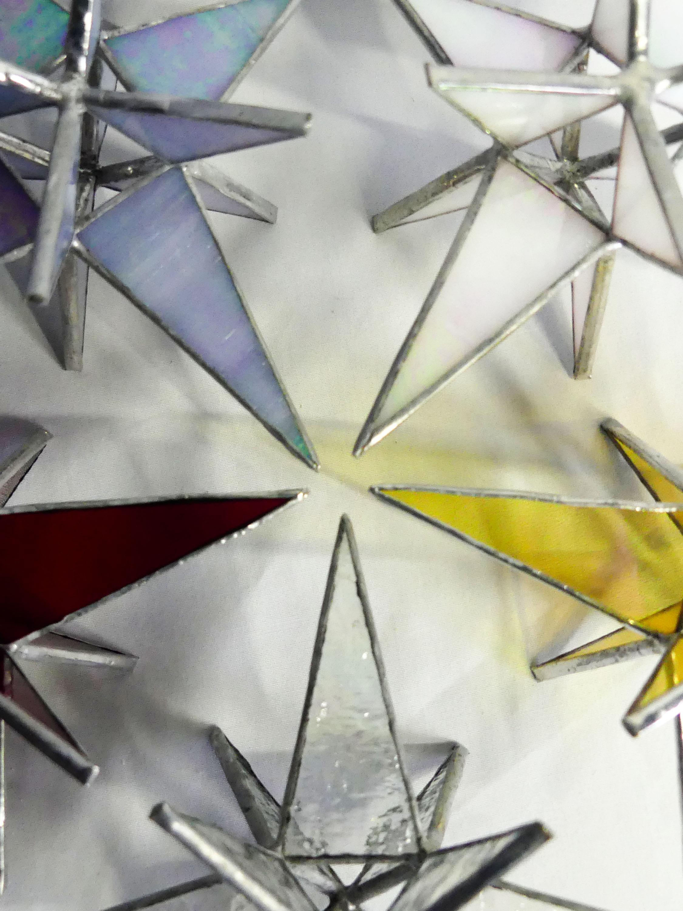 La collection Étoiles moraves rassemble des étoiles en vitrail inspirées des traditions d’Europe centrale, réalisées à la main selon la technique Tiffany. Chaque étoile est façonnée artisanalement dans mon atelier en Corrèze, à partir de verres soigneusement sélectionnés pour leurs reflets, leur profondeur et leur capacité à capter la lumière. Suspendues près d’une fenêtre, posées sur un mur ou intégrées à une décoration intérieure, ces étoiles en vitrail diffusent une lumière douce et créent une ambiance chaleureuse et poétique, de jour comme à la lueur d’une bougie ou d’un photophore. Pensées comme des objets décoratifs intemporels, elles évoquent à la fois la magie de l’hiver, les fêtes de fin d’année et une esthétique contemplative, lumineuse et artisanale. Chaque pièce est unique : les couleurs, nuances et reflets varient selon l’exposition et l’environnement, offrant une expérience lumineuse toujours renouvelée. Ces étoiles en verre sont idéales comme cadeau artisanal original, décoration murale, suspension de fenêtre ou objet symbolique, pour celles et ceux qui recherchent une création faite main, élégante et chargée de sens.