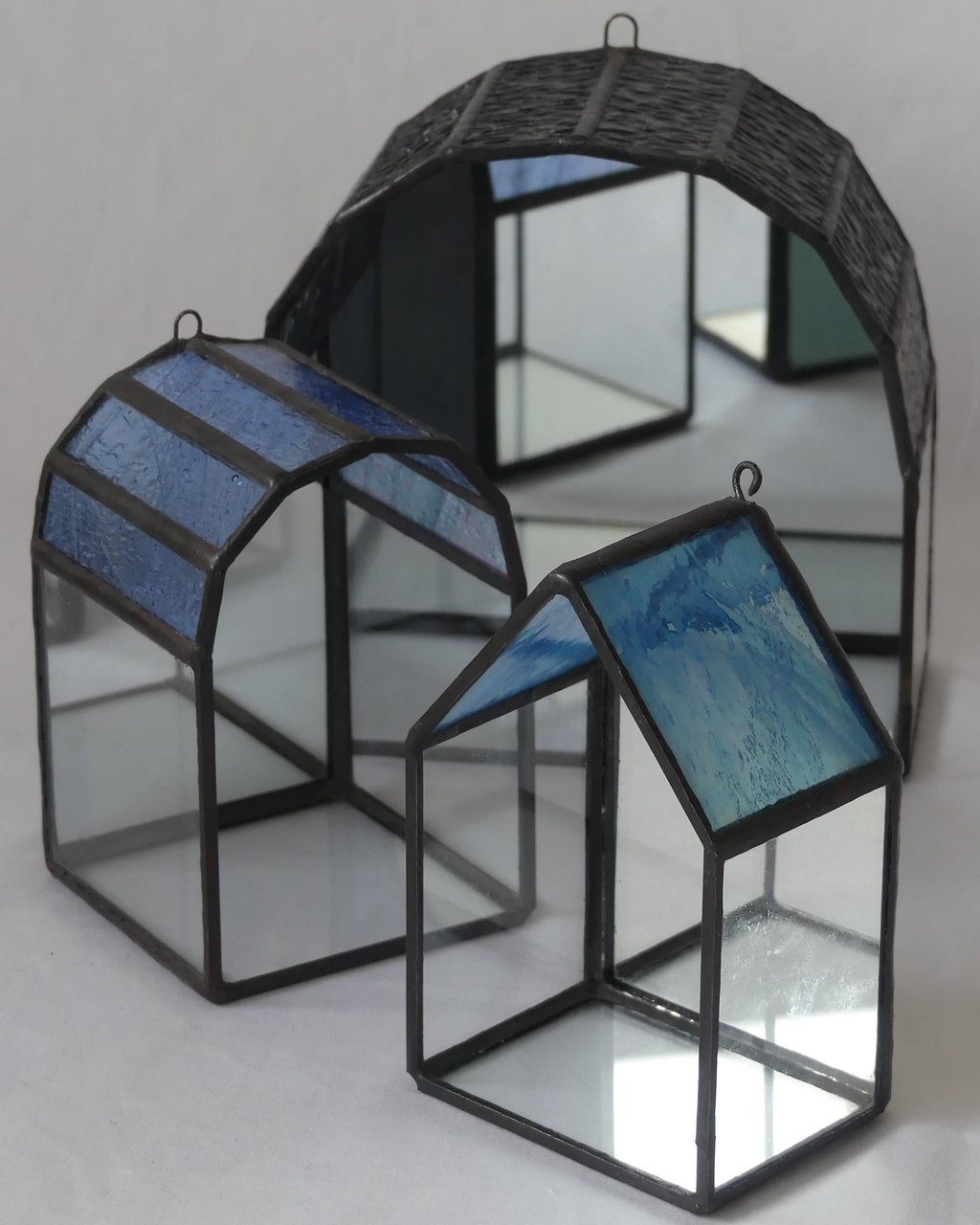 La collection Architectures intimes réunit des maisons, arches et micro-architectures en vitrail, pensées comme de petits espaces lumineux à habiter du regard. Réalisées entièrement à la main selon la technique Tiffany dans mon atelier en Corrèze, ces créations artisanales explorent la notion de refuge, de seuil et de présence intérieure. Chaque pièce peut devenir un autel personnel, le gardien d’un objet précieux ou une veilleuse diffusant une lumière douce et tamisée. À travers le verre, la lumière se fait plus intime, créant une atmosphère apaisante et contemplative. Posées sur un meuble ou suspendues contre un mur, ces architectures de verre dialoguent avec l’espace et invitent au ralentissement. Les couleurs, reflets et transparences varient selon l’environnement et l’exposition, rendant chaque création unique. La collection Architectures intimes s’adresse à celles et ceux qui recherchent une décoration artisanale sensible, mêlant vitrail contemporain, design poétique et spiritualité discrète, pour créer un lieu lumineux dédié à ce qui compte.