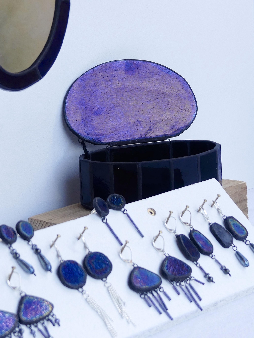 La collection Nacre noire rassemble des créations en vitrail et bijoux artisanaux inspirés par la profondeur du noir, les reflets irisés de la nacre et les phénomènes naturels liés à la lumière et au mouvement. Réalisées à la main selon la technique Tiffany dans mon atelier en Corrèze, ces pièces uniques jouent sur les contrastes entre obscurité et éclat, révélant des reflets subtils selon l’angle et l’exposition. Boîtes, miroirs, arches lumineuses et boucles d’oreilles composent une collection à la fois décorative et contemplative, pensée comme une exploration de la matière, de la lumière et du silence. Le verre noir irisé capte la lumière avec discrétion, évoquant la nacre, les astres, la pluie ou les phénomènes célestes, tandis que chaque création transforme l’espace par une présence douce et élégante. Les nuances et reflets varient naturellement selon l’environnement, rendant chaque pièce véritablement unique. La collection Nacre noire s’adresse à celles et ceux qui recherchent un objet artisanal fait main, à la fois sobre, poétique et raffiné, mêlant vitrail contemporain, design sensible et inspiration naturelle, pour une décoration ou un bijou lumineux et intemporel.