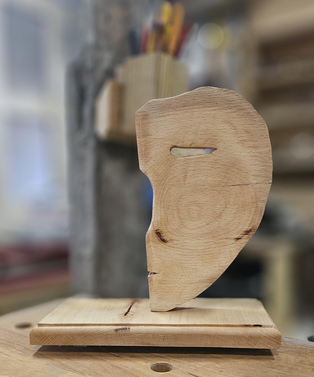 photo d'un masque sculpté a la main représentant un demi visage sur support en bois naturel et massif