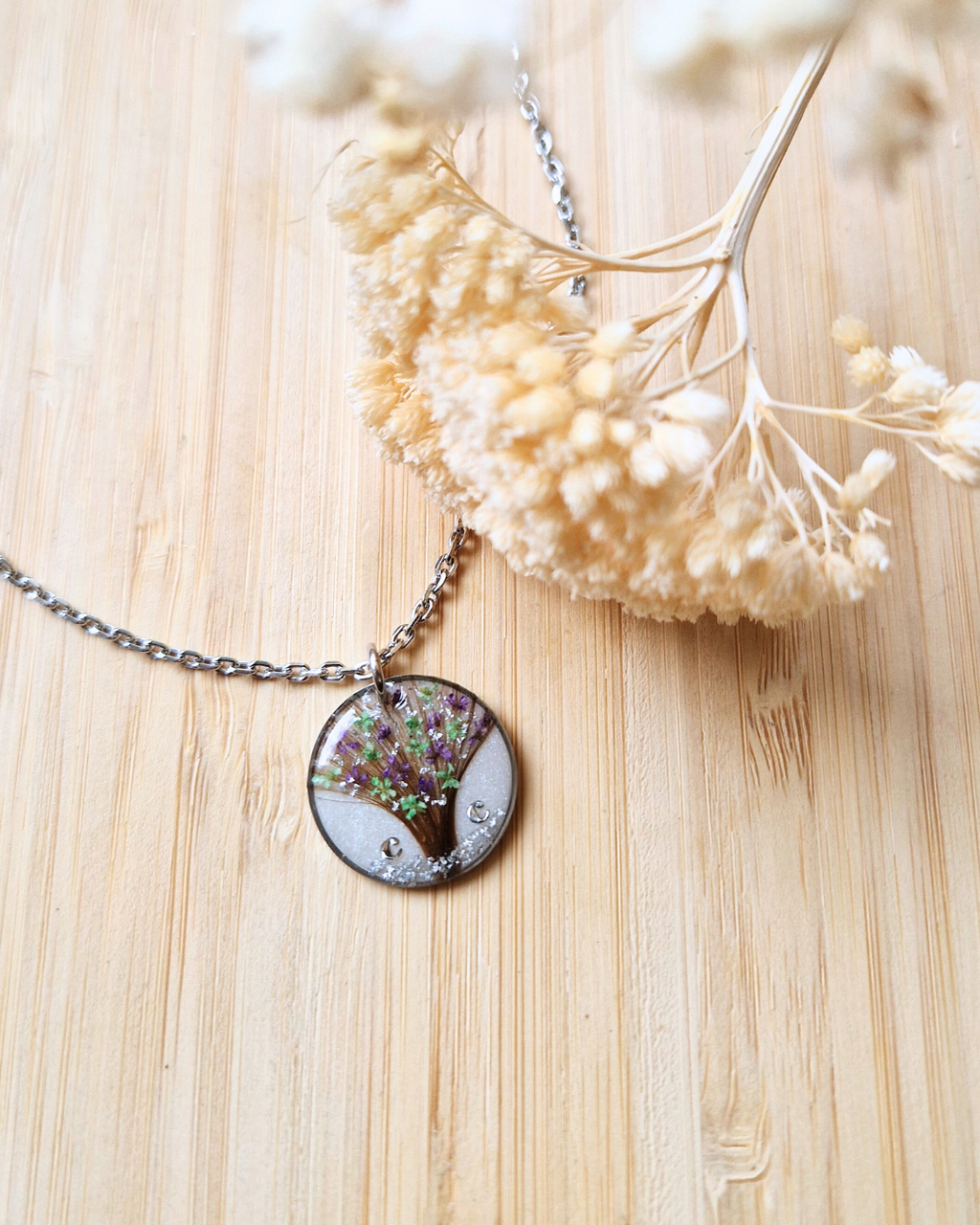 Collier souvenir personnalisé avec mèche de cheveux d’enfant, fleurs séchées, initiale et feuille argentée sur fond blanc nacré