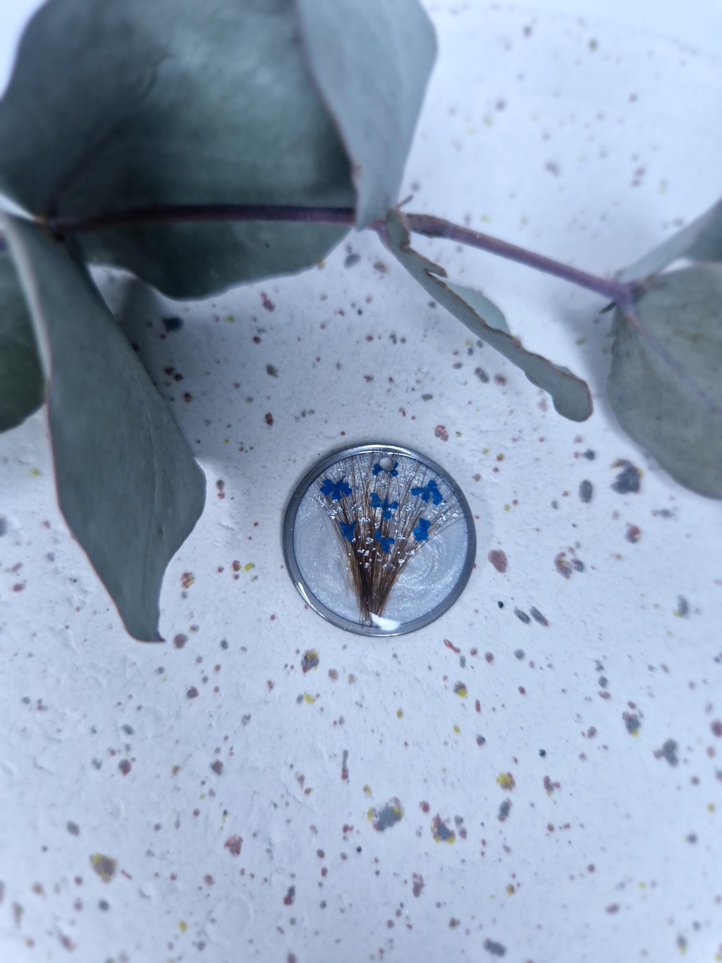 Collier souvenir personnalisé avec mèche de cheveux, fleurs séchées et feuille argentée sur fond blanc nacré