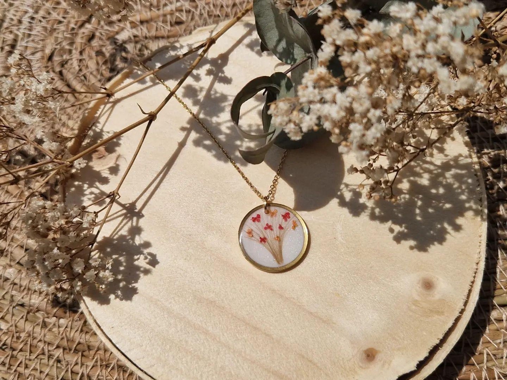 Collier souvenir personnalisé avec les mèches de cheveux de jumelles, fleurs séchées et feuille dorée sur fond blanc nacré