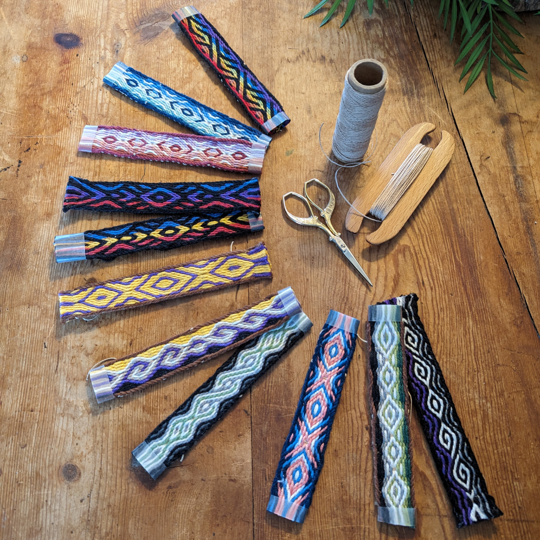 photo d'un ensemble de galons tissés étalés en éventail sur ma table de travail avec quelques petits outils de tissage