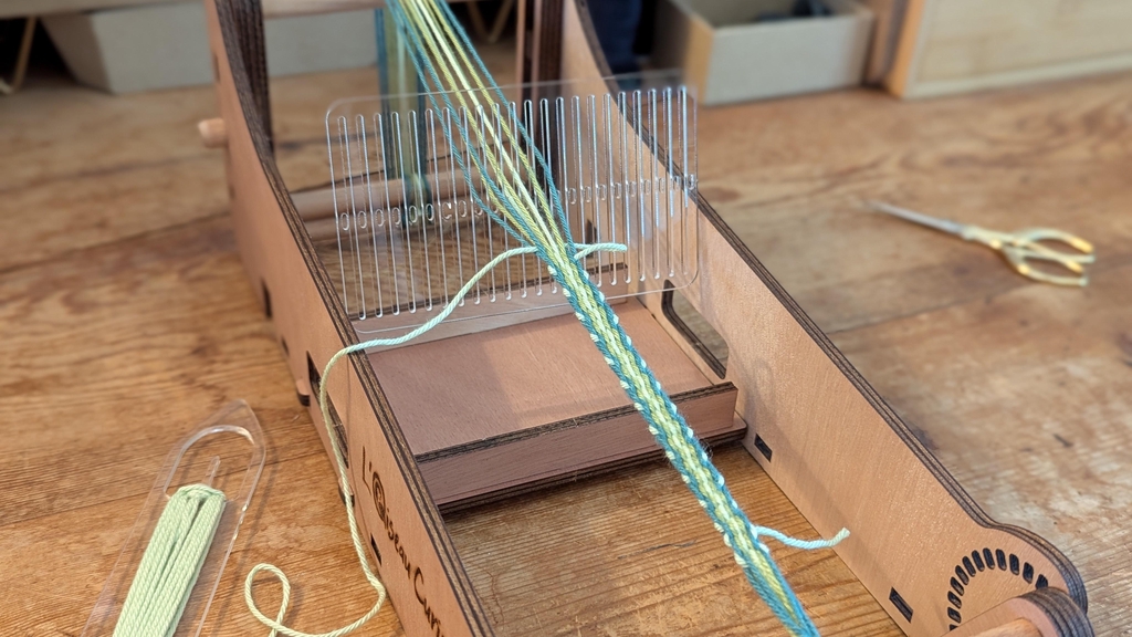 Photo de métier à tisser posé sur une table en bois avec petit cordon en cours de tissage