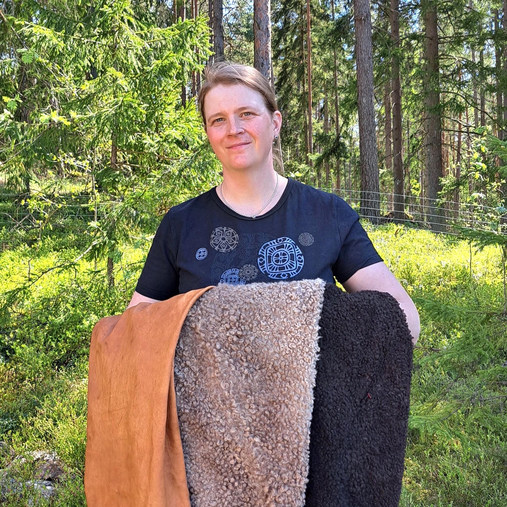 Naskaliinan yrittäjä metsässä perinteisin menetelmin parkitut nahkavuodat sylissä.