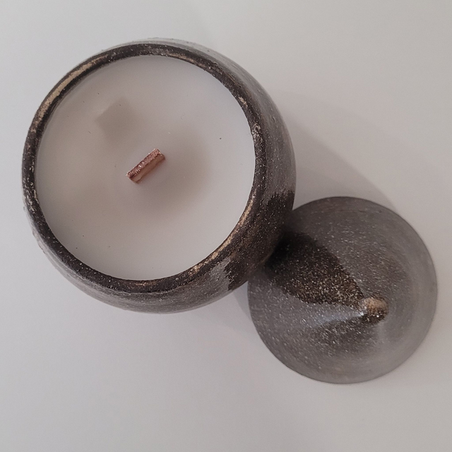 Bougie en grès façonnée au tour, composée d’un contenant et d’un couvercle en forme de goutte d’eau.
 Chaque pièce explore les contrastes de matière entre mat et brillant, lisse et texturé.
Coulée à la main en cire d’abeille naturelle non parfumée, elle est équipée d’une mèche en bois qui offre une flamme douce et légèrement crépitante.
Chaque bougie est unique, issue d’un travail de matière, de cuisson et de surface.