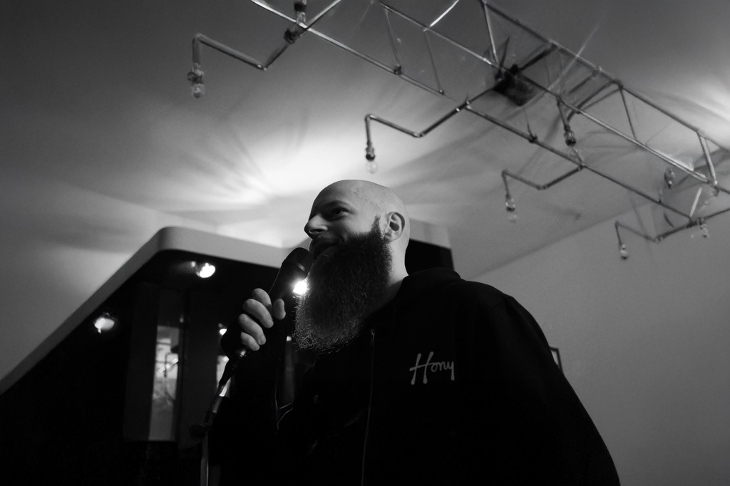 Der Grafikkünstler Hony steht in einem Lokal und hält ein Mikrofon in der Hand.