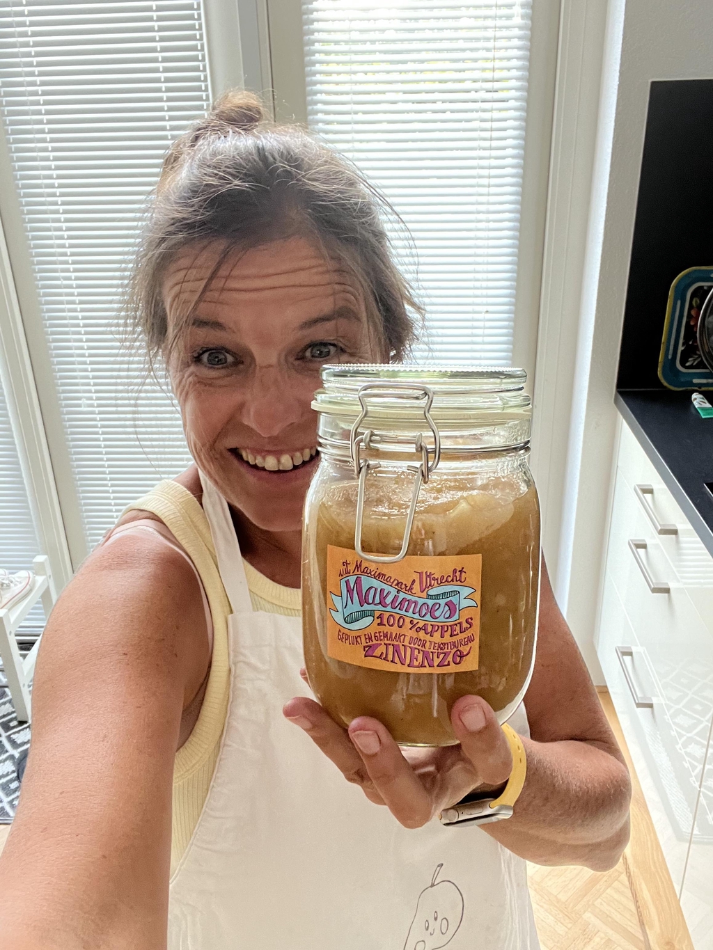 Appelmoesmaker Esther de Hek houdt een grote glazen pot Maximoes Appelmoes vast, met kleurrijk etiket waarop '100% appels' en 'uit Máximapark Utrecht' staat vermeld.