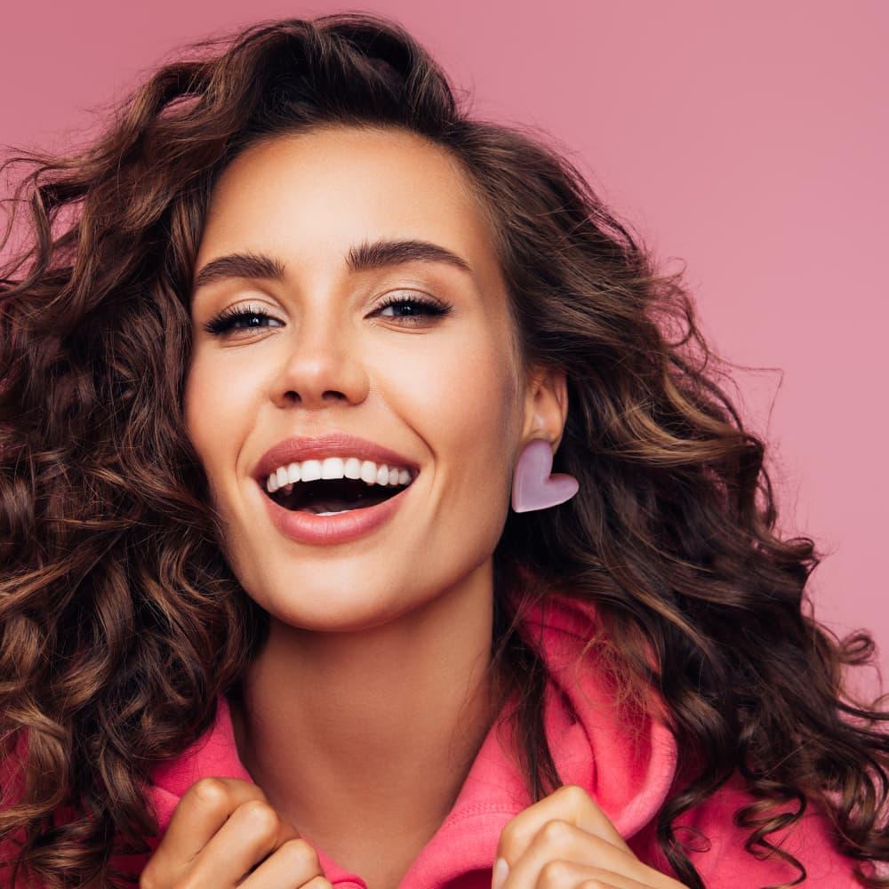 femme brune contente avec des boucles d'oreilles en forme de cœur rose faits main, bijoux créateur de la marque Flowerinlife