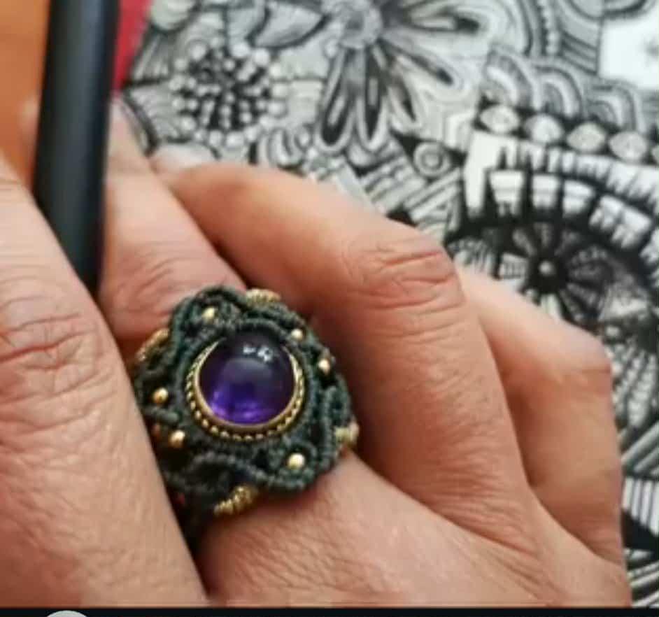 Main de la créatrice Slowfil portant une bague artisanale en micromacramé tissée à la main avec une pierre naturelle d'améthyste violette.