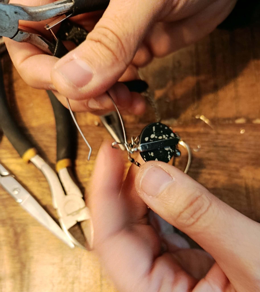 Mains de l'artisane Slowfil démontant avec précision un bijou ancien pour en récupérer les perles et apprêts destinés à une nouvelle création upcyclée.