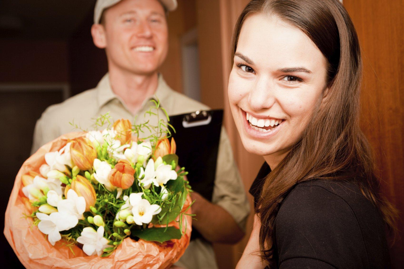 Blumenversand und Lieferservice. Übergabe eines Blumenstraußes vom Lieferfahrer an eine Empfängerin (Bildbeschreibung)