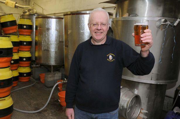 The owner, Paul Bardsley, holding a pint of beer in front of the brewery fermenters.