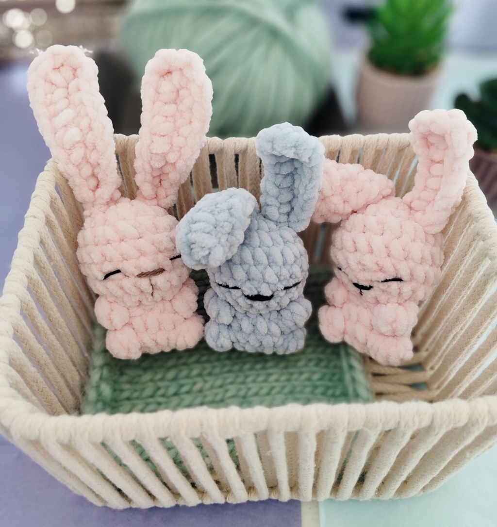 Trois petits lapins crochetés en fil chenille très doux, en couleurs pastels dans un panier. Illustration des créations douces et uniques de Le Monde d'Anastasiia