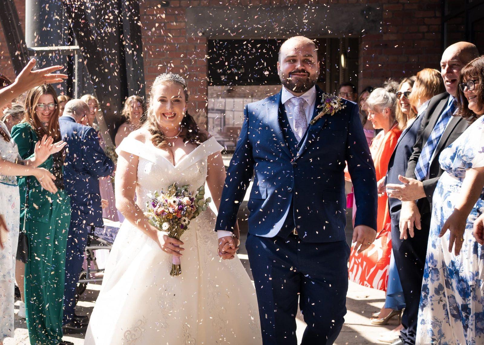 Newly married couple in confetti holding a dried flower bouquet