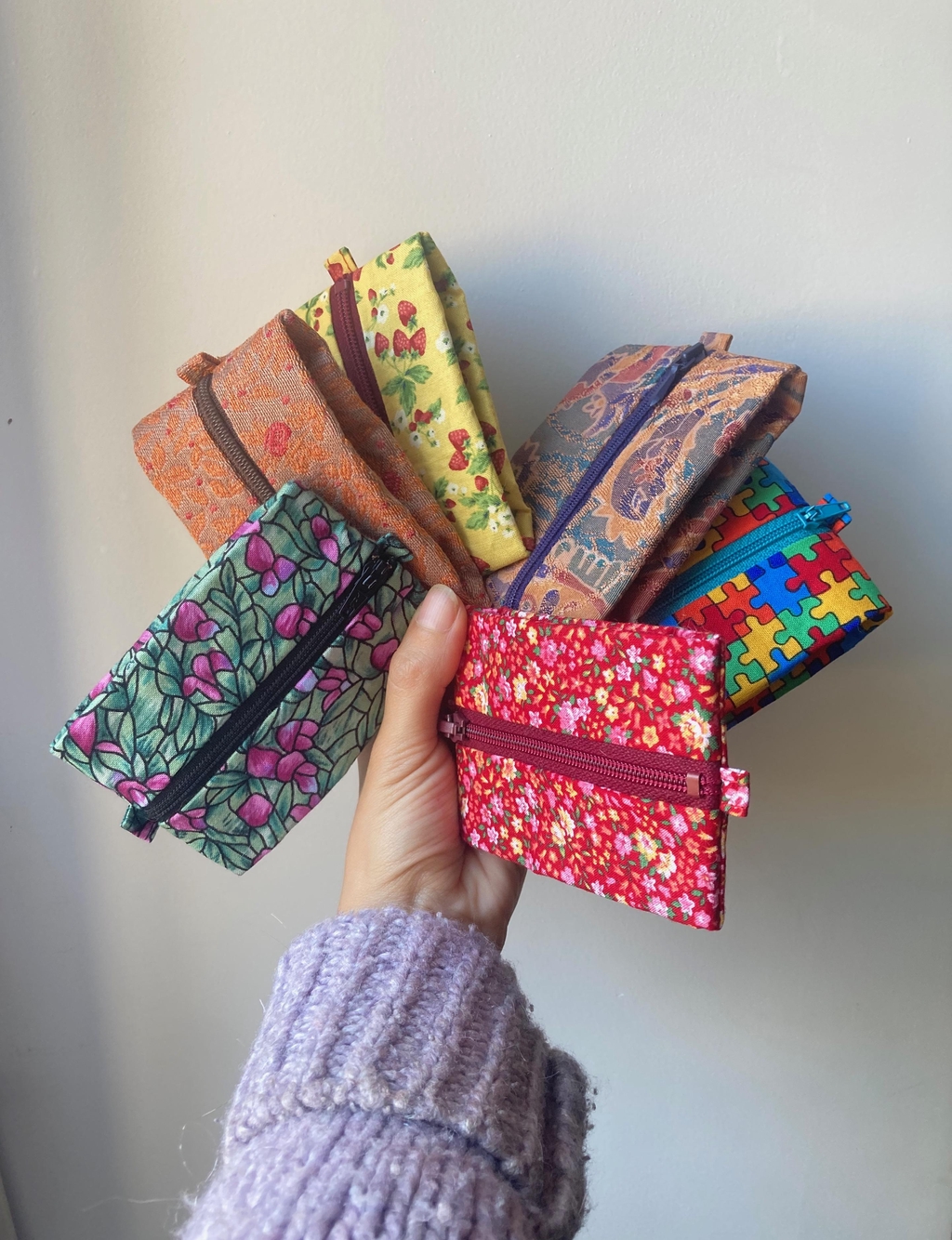 Image d'une main tenant six porte-monnaie en tissus colorés.