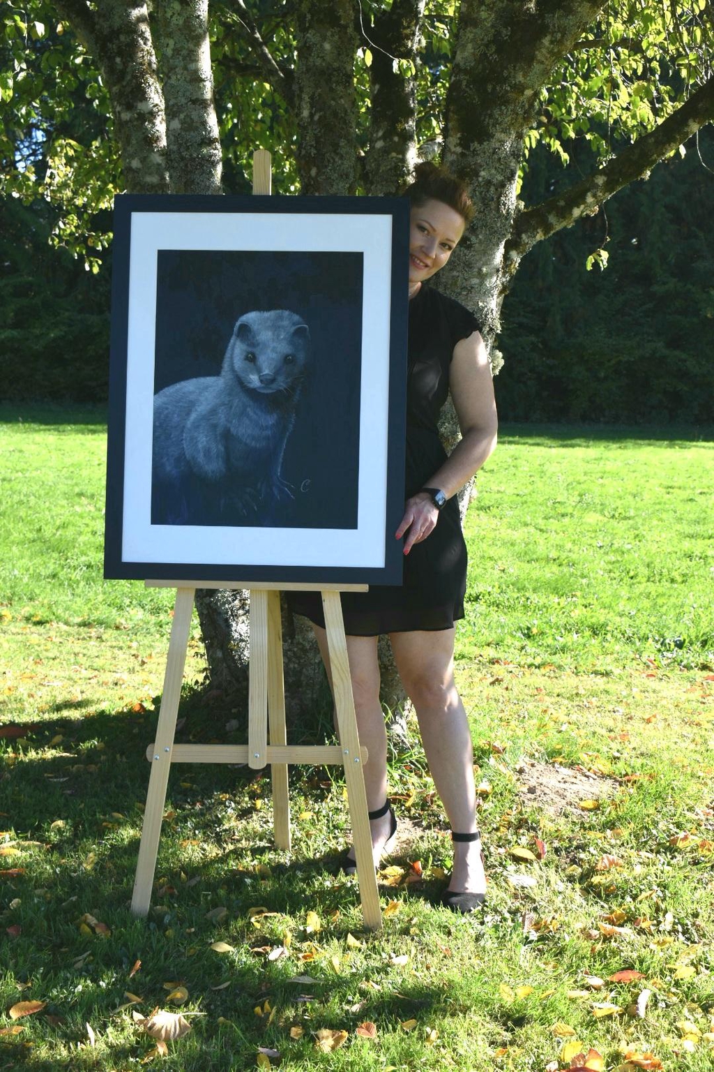 Oeuvres du Vison d'europe prise en photo encadrée. La photo est prise en extérieur avec à l'arrière l'artiste Cécilia PELISSIER et la nature