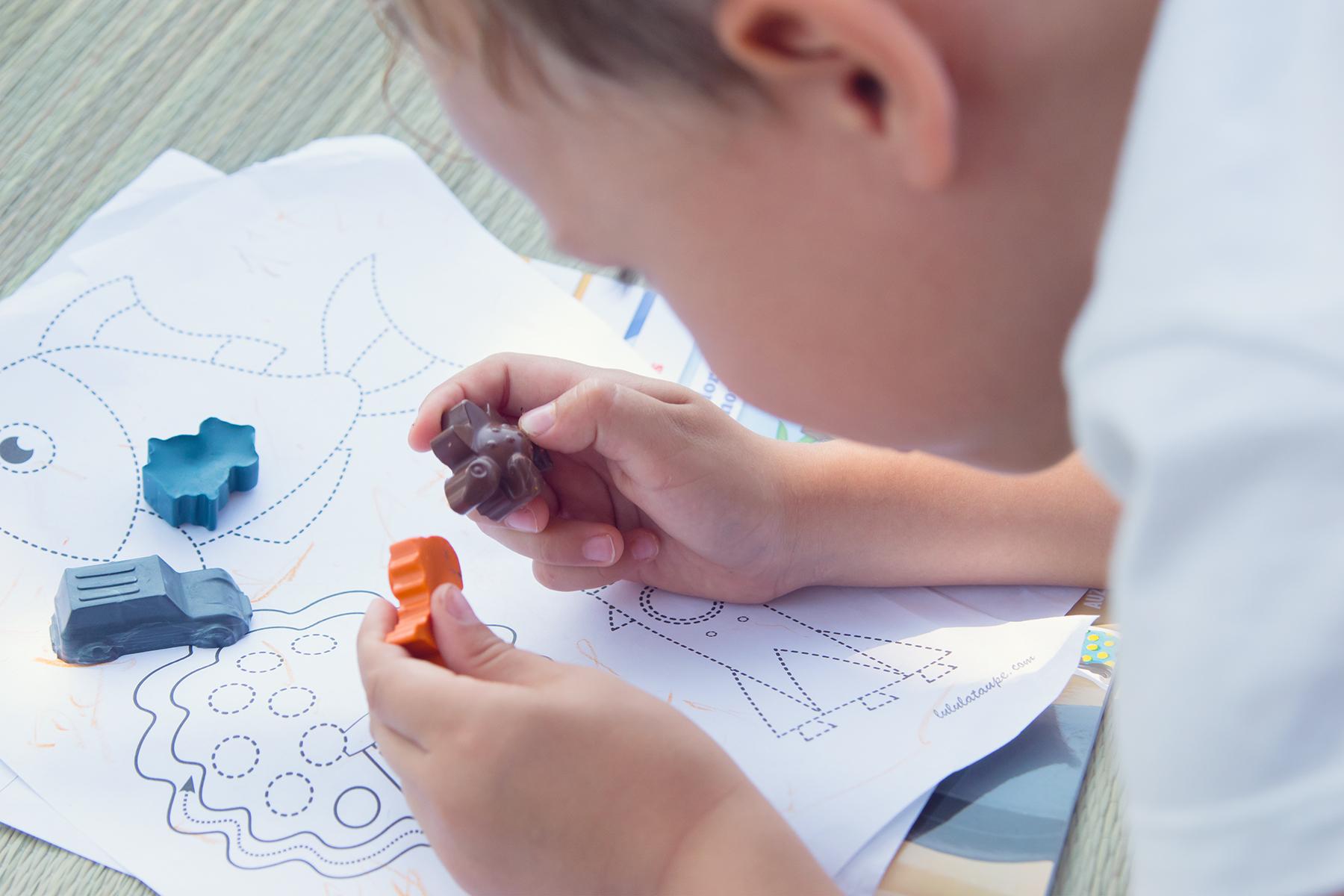 mains d’enfant de cinq ans jouant avec des crayons en forme de dinosaure sur une feuille blanche de coloriage