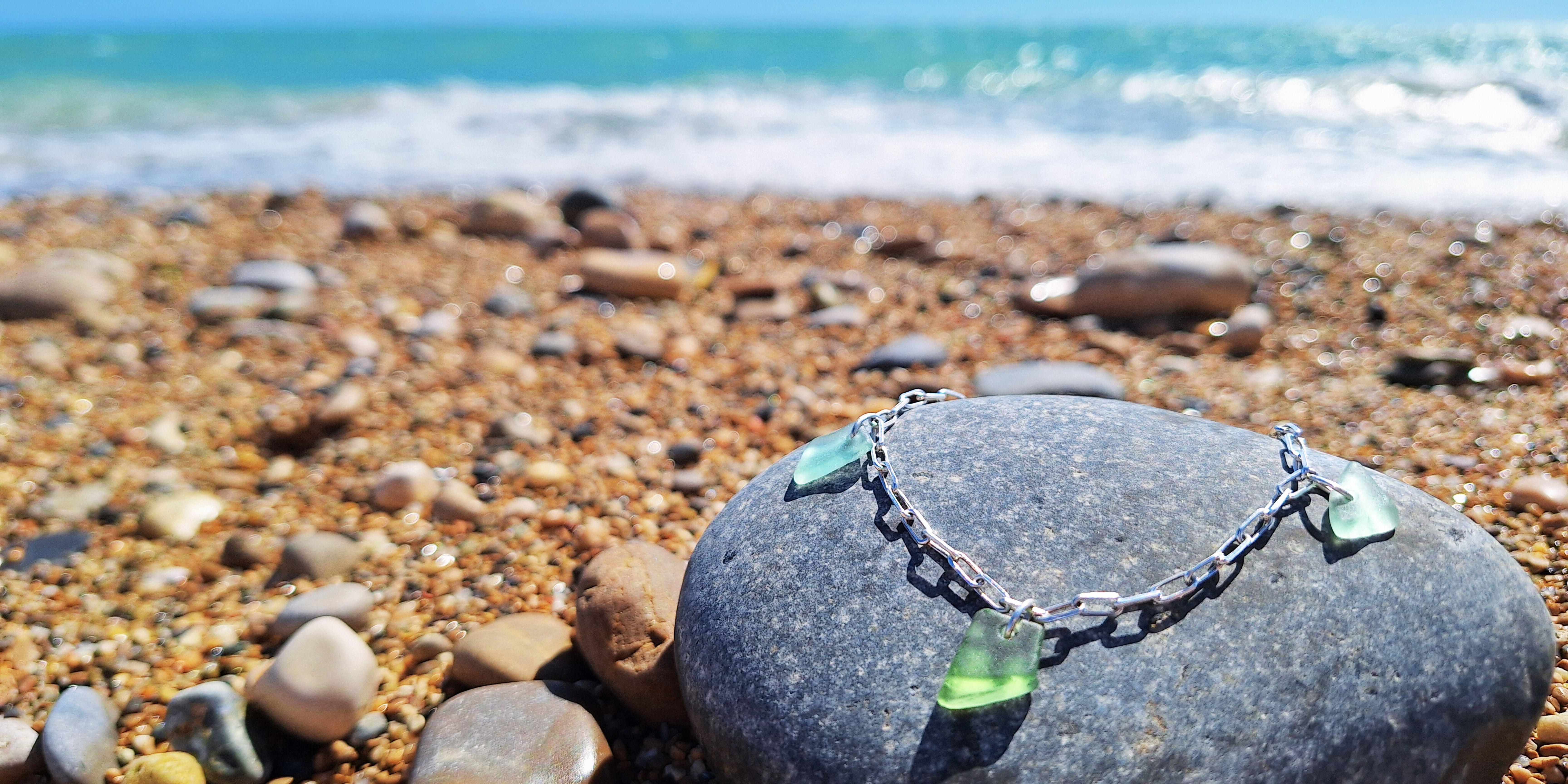 beach glass silver bracelet on stone beach turquoise sea waves in background