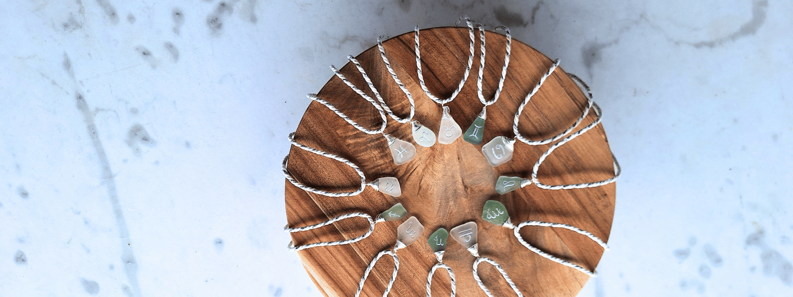 beach glass pendants with astro signs placed in circle on wooden tray
