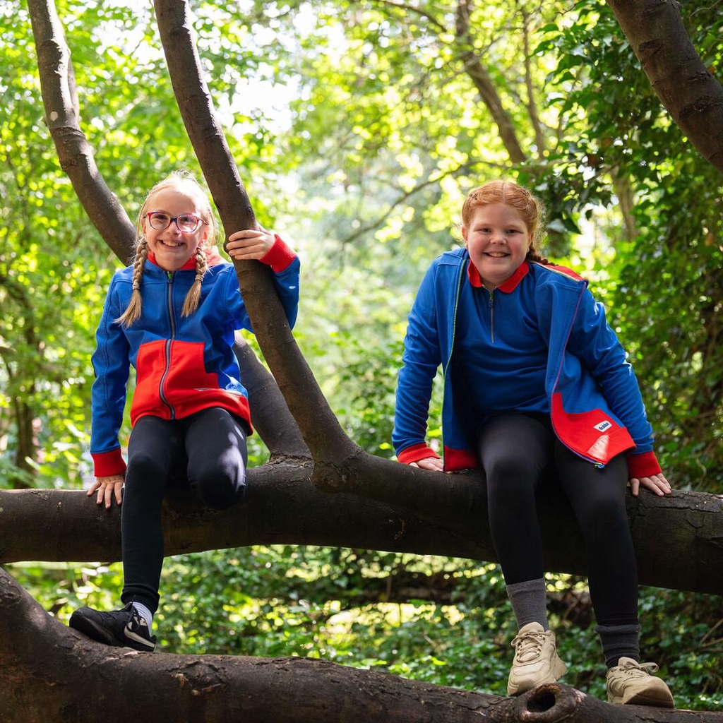 Phot of two Guides sitting on the branch of a tree, smiling, wearing their Guide uniform.