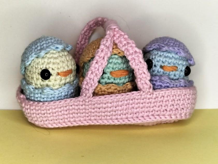 Un assemblage de la collection de Pâques, 3 poussins de couleur ivoire, vert blanc et bleu ciel clair avec des déguisements coquilles bleu ciel clair, orange pastel et lilas clair dans un panier rose