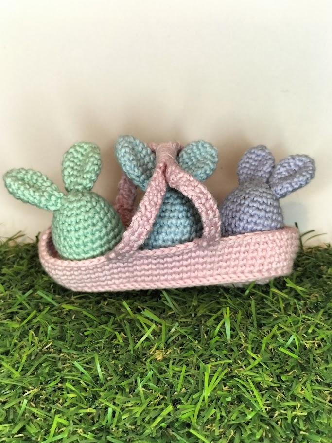 Un assemblage de la collection de Pâques, 3 oeufs lapins vert blanc, lilas clair et bleu clair dans un panier rose.