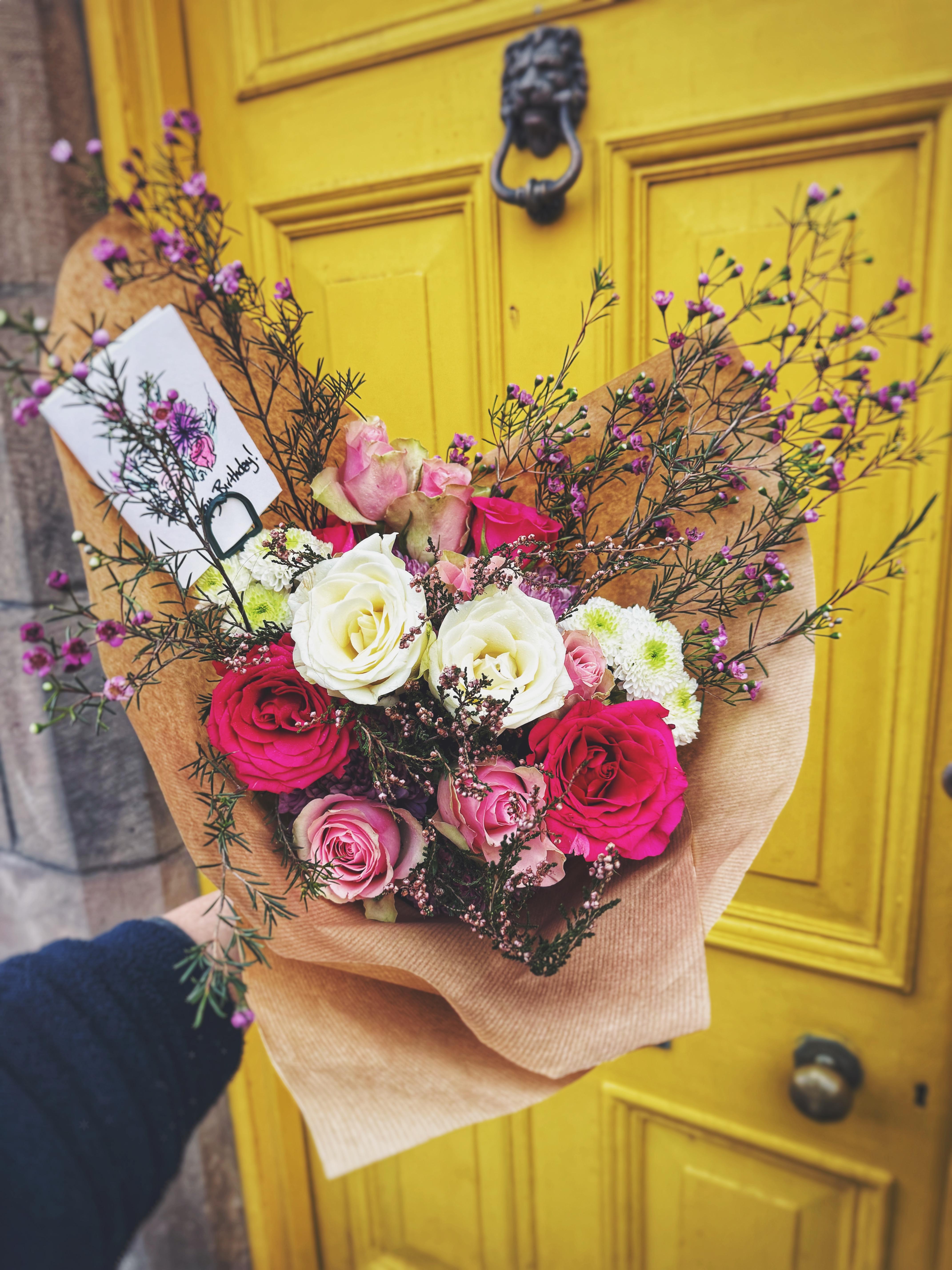 A rose and wax flower handtied bouquet in front of a yellow door