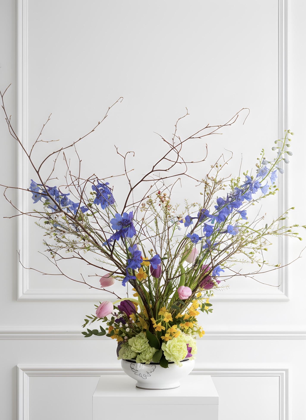 A porcelain bowl filled with spring flowers and tall twigs