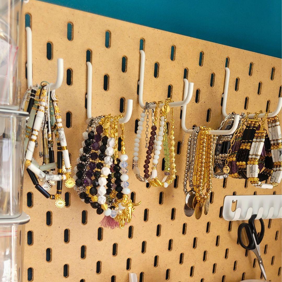 Photo des bijoux finalisés, suspendus aux crochets de l'atelier de la créatrice. Chaque pièce, unique et soigneusement réalisée à la main, reflète la production en petite quantité de la marque, sans stock disponible. Cette image met en avant le processus artisanal et l'exclusivité des créations, conçues avec soin et inspirées par la nature, pour ceux qui recherchent des bijoux uniques