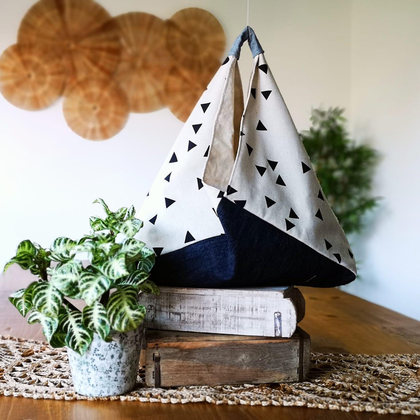 Sew She Did market bento bag made with natural cotton canvas remnant bearing black geometric pattern and denim. Placed on a wooden table next to a green house plant.
