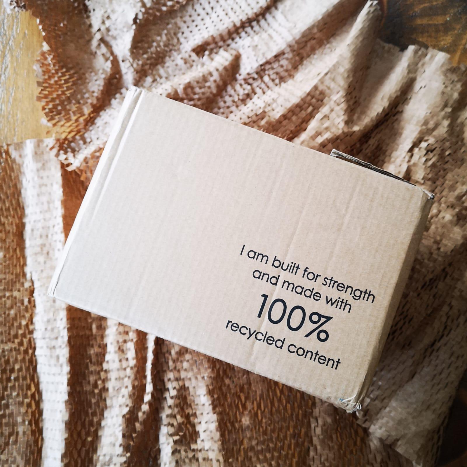 A battered cardboard box with a slogan printed on it "I am built for strength and made with 100% recycled content". It is sat on kraft paper packaging.