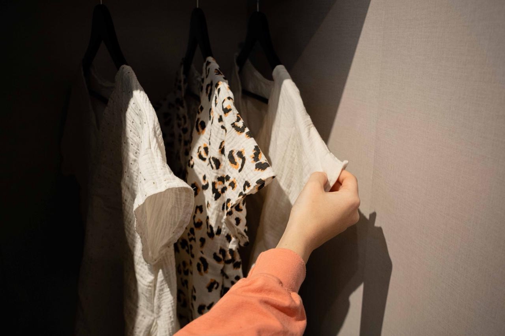 Trois pyjamas dans une armoire : l'un à poids, l'autre léopard, l'autre crème ou écru. Une main montre le pyjama. 