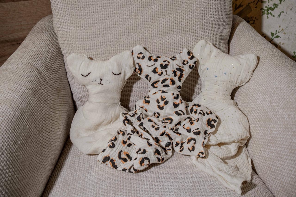 Trois petits doudous au visage brodé à la main sont sur un fauteil.